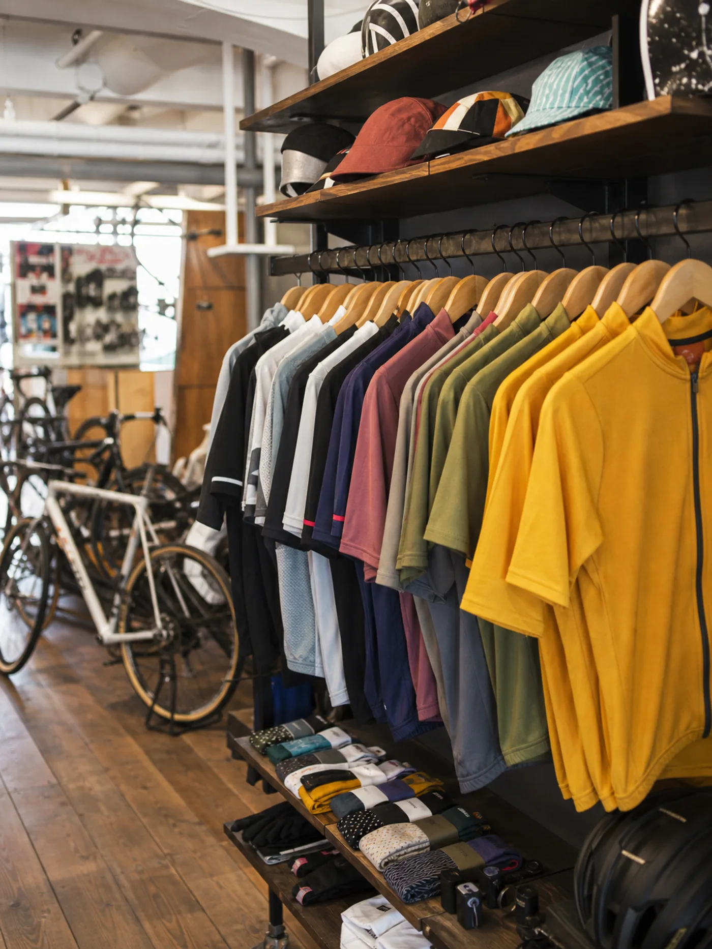 Cycling jerseys hanging in graduated colours on a bike shop rail with a road bike parked alongside