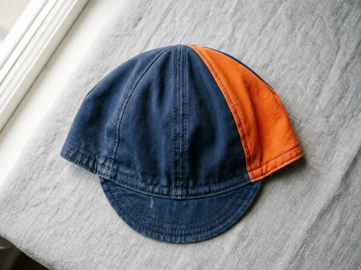A cycling cap laid flat on a plain surface, navy crown with contrast orange panel