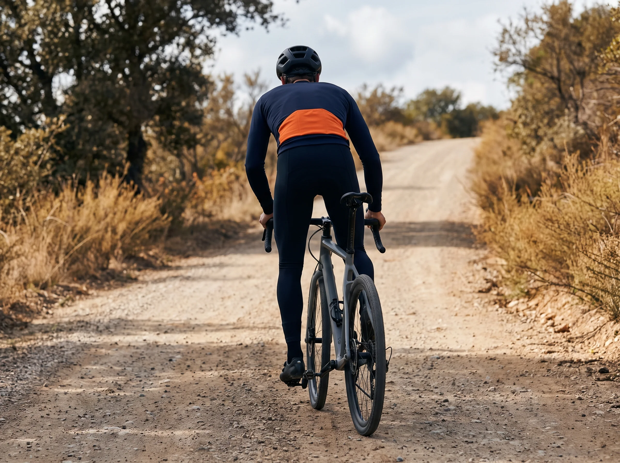 Rider out of the saddle on a gravel climb, shoulders and upper back working through the stroke