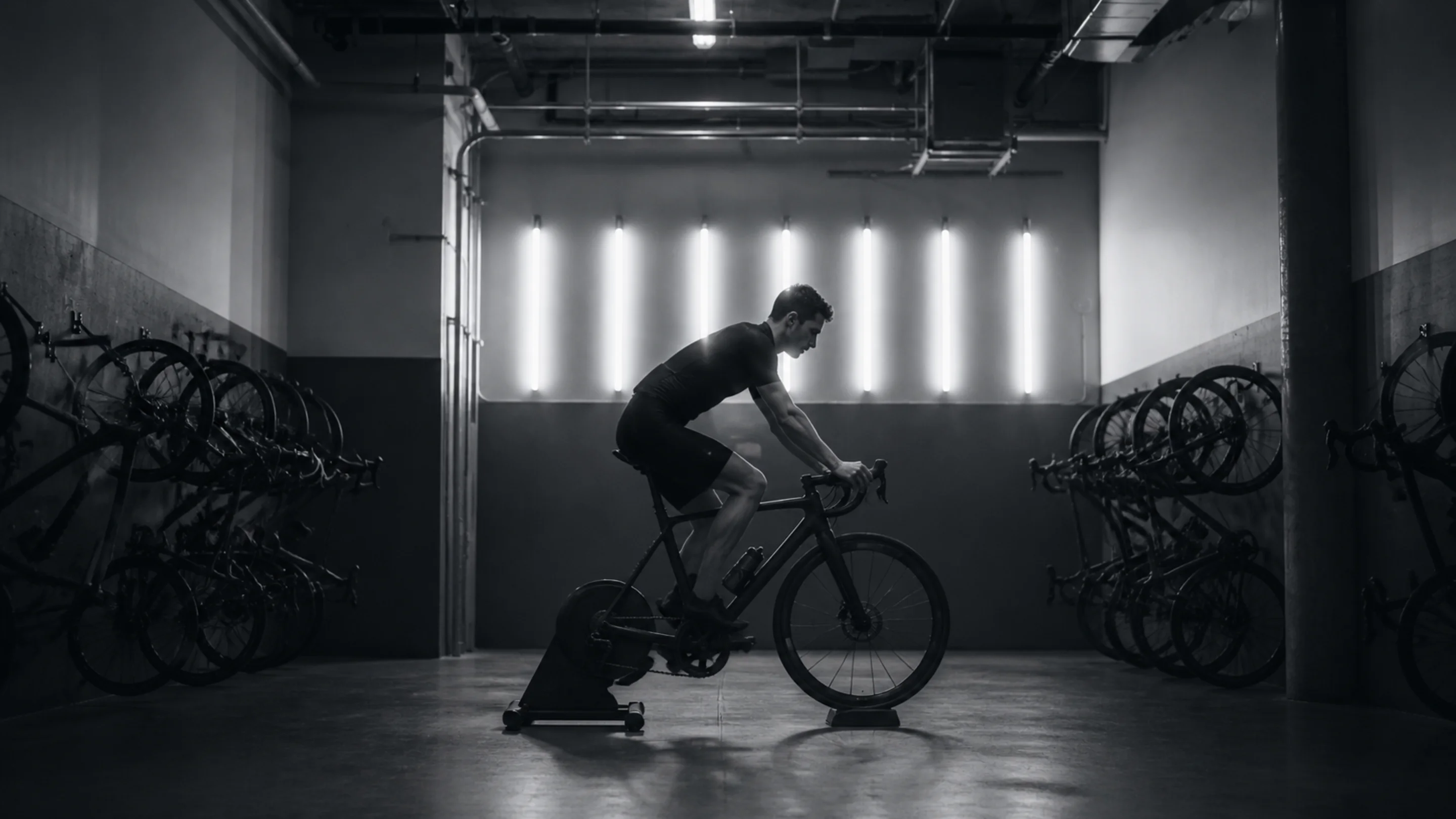 Symmetric indoor cycling studio, bikes and fluorescent light fixtures in a dark, backlit room
