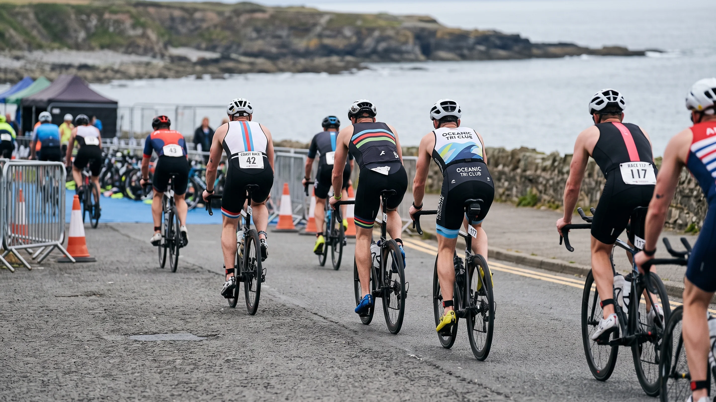 Triathletes riding out of a transition area on a coastal race course