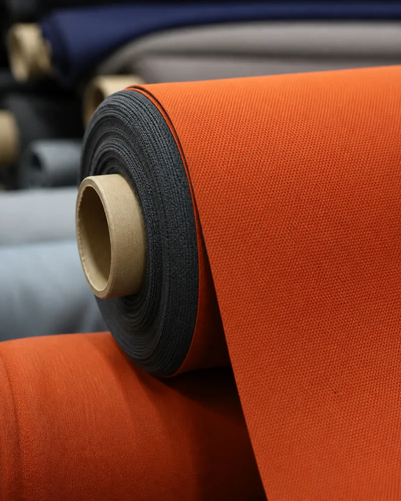 An orange fabric roll on a cutting table beside darker rolls on a mill floor