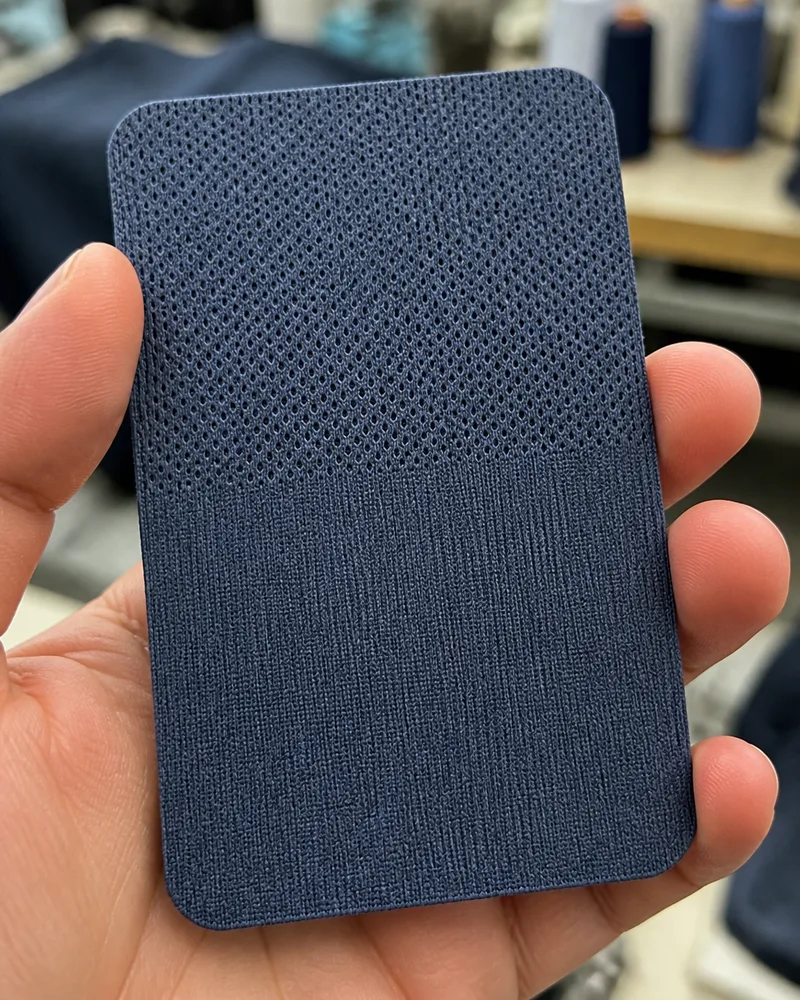 A hand holding a navy textured technical swatch with a dot-structure knit visible