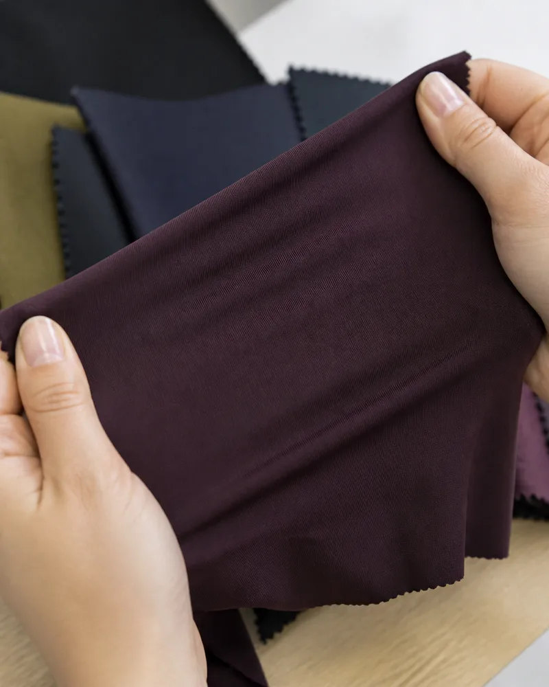 A hand lifting a maroon swatch from a stack of colour options on a worktable