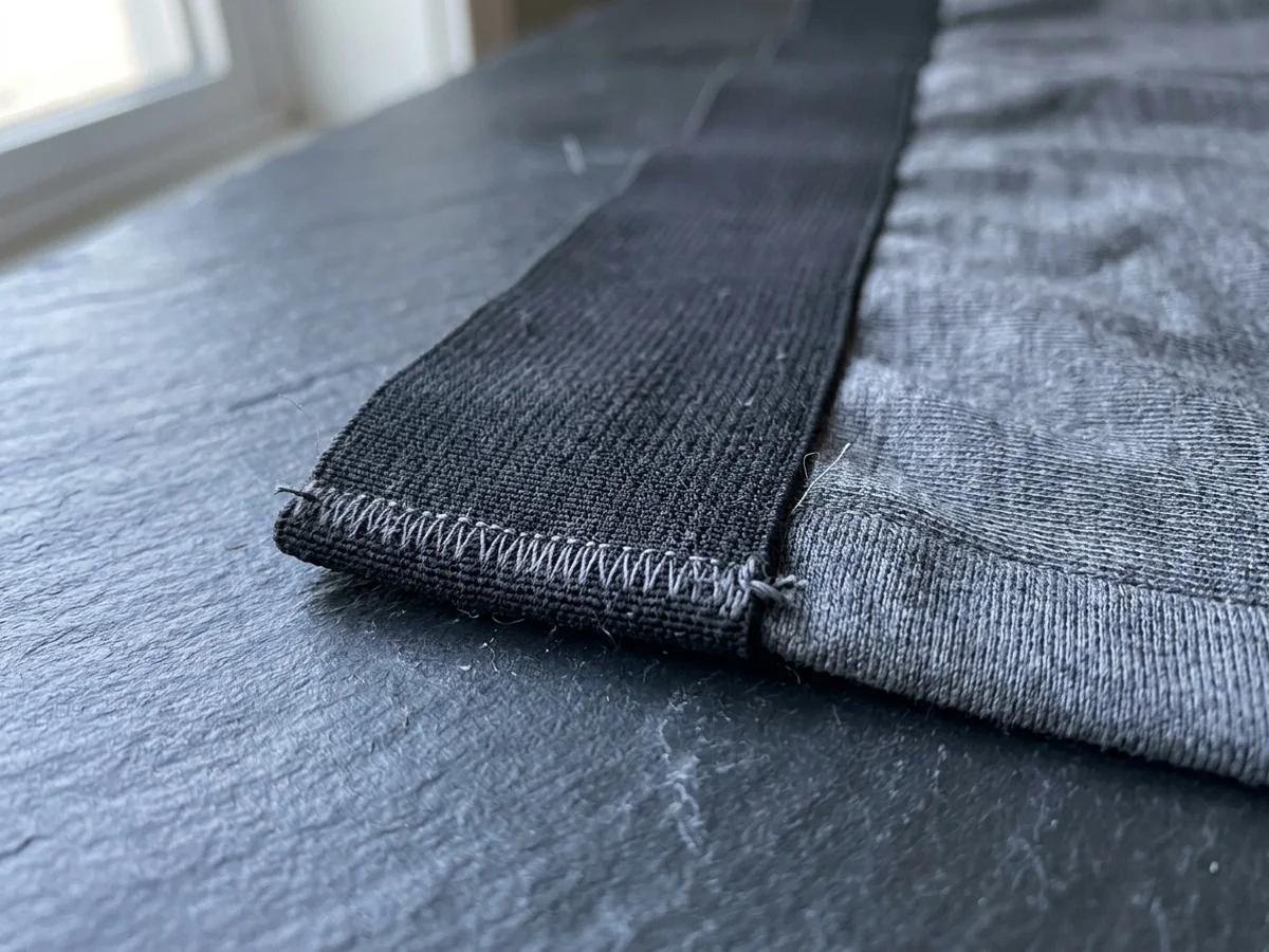 Extreme macro of the coverstitched terminating end of a flat elastic band on grey performance knit