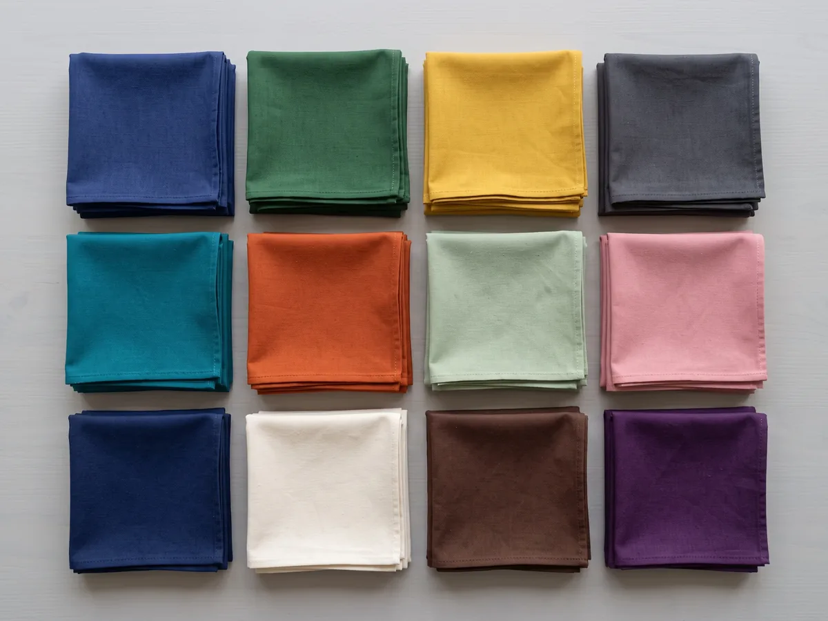Folded pieces of dyed cloth in several colours, each with a bound edge, laid overlapping