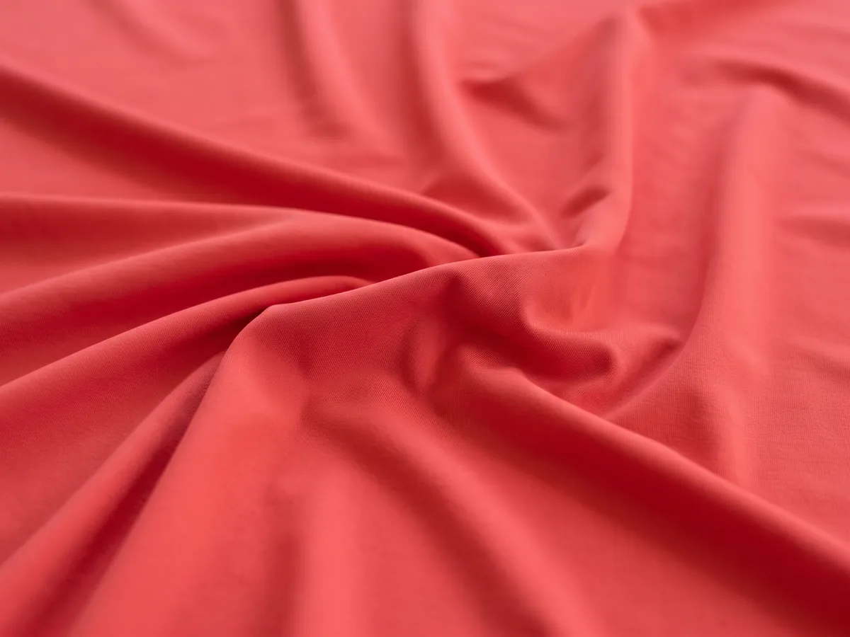 A smooth coral-red stretch fabric in soft folds