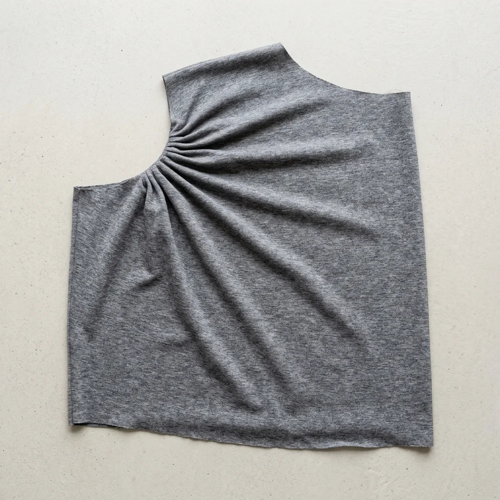 The same panel shaped with an armhole curve, gathered fullness radiating from that one upper corner